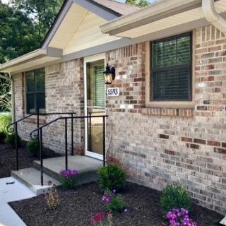 A charming brick house with a small porch and garden featuring flowers.