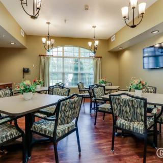 A well-lit dining room with multiple tables and chairs, featuring elegant chandeliers and a large window.