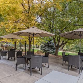 Outdoor patio area with tables, chairs, and umbrellas under autumn trees.