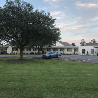 A car parked in front of a single-story building with a large tree nearby on a cloudy day.