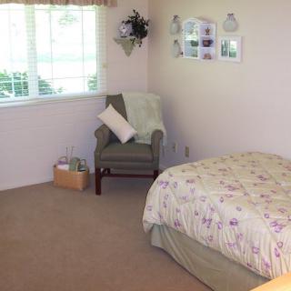 A cozy bedroom with a bed, an armchair, and a window letting in natural light.