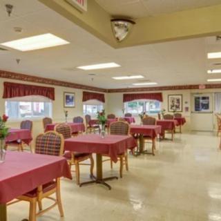 An empty dining room with neatly arranged tables and chairs, featuring red tablecloths and decorative accents.