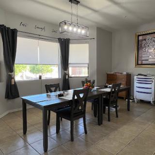 A modern dining area featuring a table with black chairs, stylish lighting, and large windows adorned with curtains.