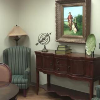 A cozy corner with a classic armchair, a table adorned with decorative items, and an artwork hanging on the wall.