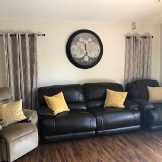 A cozy living room with a leather sofa, recliner, and large wall clock.