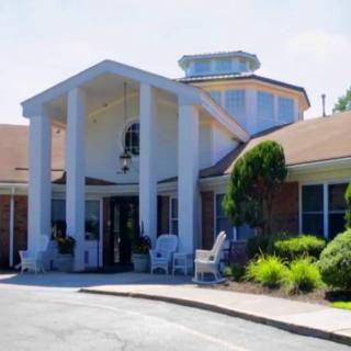 A front view of a building with a prominent entrance and white columns surrounded by greenery.