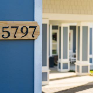 A house with the visible address number 5797 displayed on a wooden plaque, showcasing part of the home's exterior and porch area.