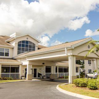 A modern building with a covered entrance and driveway under a partly cloudy sky.