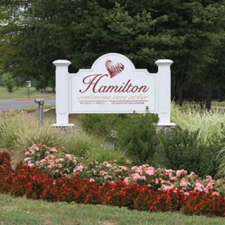 A welcoming sign for Hamilton surrounded by a well-maintained garden with flowers.
