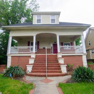 A two-story house with a large porch and brick steps leading up to the entrance.