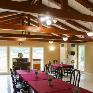 A cozy dining area featuring tables dressed with red tablecloths, wooden beams overhead, and ample natural light.