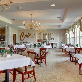 An elegant restaurant dining area with neatly arranged tables and chairs, adorned with chandeliers and large windows.