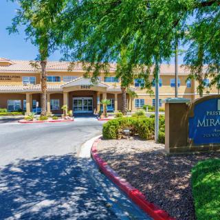 The entrance to a hotel surrounded by well-maintained landscaping and trees on a sunny day.