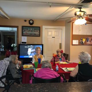 A group of seniors socializing around a table with a television in the background.