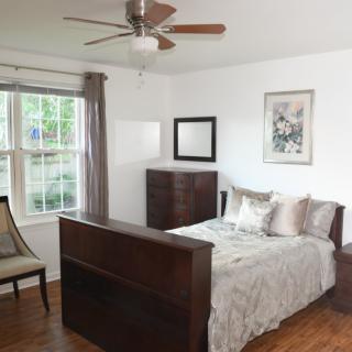 A cozy bedroom with a bed, dresser, chair, and ceiling fan.