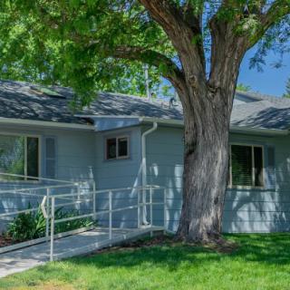 A residential house with a wheelchair ramp and a large tree in the front yard.