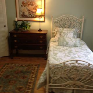 A cozy bedroom with a single bed and nightstand, adorned with decorative pillows, a lamp, and a painting on the wall.
