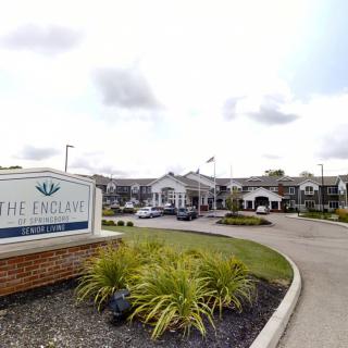 Entrance of a large building complex with a sign and landscaped driveway.