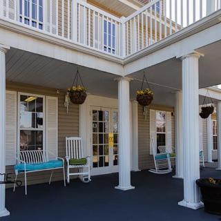 A cozy porch with white columns, featuring chairs and hanging plants.