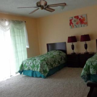 A cozy bedroom featuring two twin beds with green bedding, adorned with matching lamps and a colorful painting above the headboards.