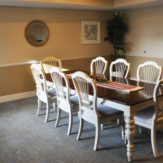 A neatly arranged dining room with a long table and eight chairs, featuring wall decorations and a mirror.