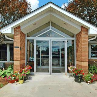 A modern building entrance with brick pillars and glass doors, surrounded by plants and landscaping.