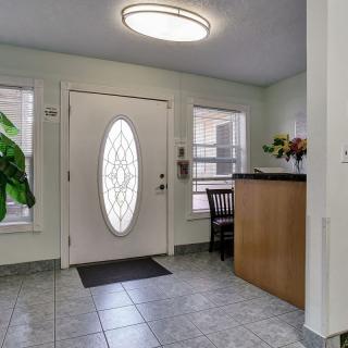 A bright foyer with a tiled floor and an oval glass door, featuring plants and a small desk.