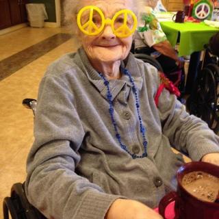 An elderly person wearing peace sign glasses enjoys a drink, embracing a fun and colorful atmosphere.