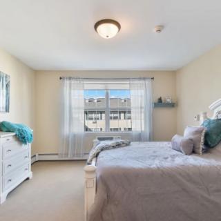 A bright and cozy bedroom featuring a bed, dresser, and large window.