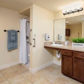 A clean and organized bathroom featuring a large mirror, sink, shower area, and neatly hung towels.