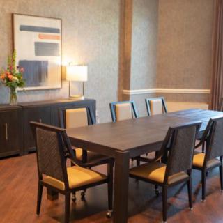 A well-furnished dining room with a large table, several chairs, a sideboard with a lamp, and wall artwork.