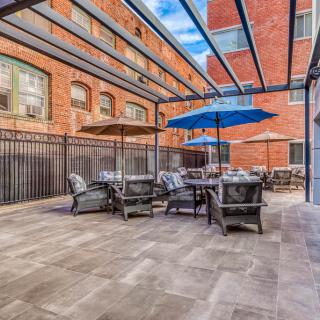 A modern outdoor patio area with tables, chairs, and umbrellas, set against a brick building backdrop.