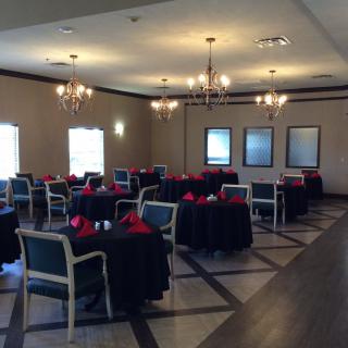 A dining area with elegant chandeliers, neatly arranged tables covered in black tablecloths and red napkins.