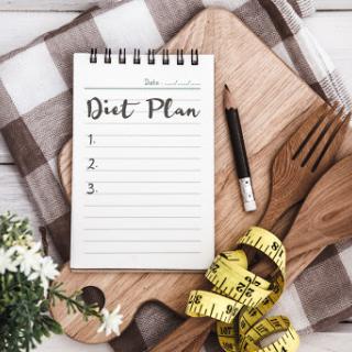 A tidy diet plan notebook ready for meal planning with wooden utensils and a tape measure.