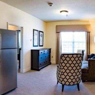 A well-furnished living room with a refrigerator, seating area, and natural light from the window.