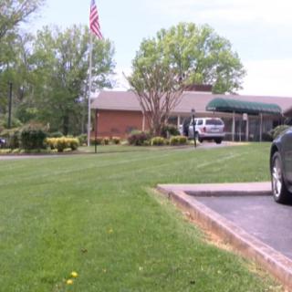A building with a well-maintained lawn and a parked car, accompanied by an American flag, surrounded by trees.