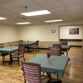 A spacious dining area with neatly arranged tables and chairs, featuring green tablecloths and a warm wooden floor.