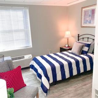 A cozy bedroom with a single bed featuring striped bedding and a bedside lamp, complemented by modern decor.