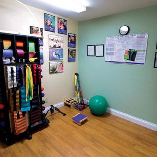 A small exercise room equipped with yoga mats, resistance bands, a stability ball, and motivational posters on the walls.