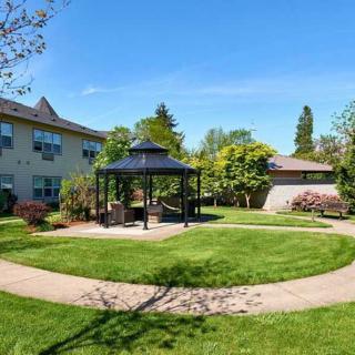 A peaceful garden with a central gazebo, surrounded by lush green lawns and trees on a sunny day.