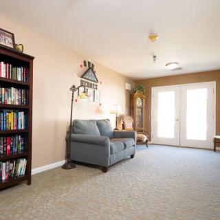 A cozy living room with a bookshelf, sofa, and artwork, featuring soft lighting and double doors leading outside.