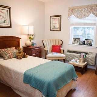 A cozy bedroom with a single bed and warm decor, featuring a chair by the window.