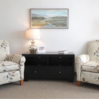 A cozy living room setup featuring two floral armchairs, a dark side table with a decorative lamp, and a landscape painting on the wall.