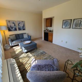 A cozy living room with a sofa, coffee table, and warm lighting from a standing lamp. Artwork decorates the walls, creating a relaxing atmosphere.