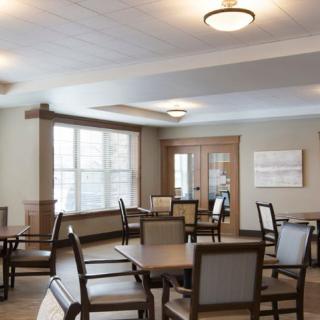 A spacious dining area with several tables and chairs, illuminated by ceiling lights, and featuring large windows.