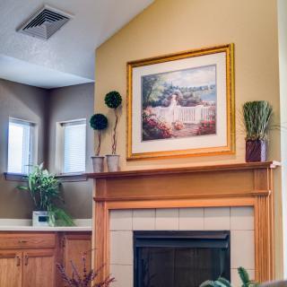 A cozy living room with a fireplace, adorned with plants and a framed painting above the mantel.