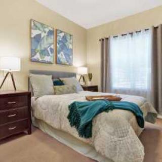 A cozy bedroom with a neatly made bed, adorned with colorful artwork and elegant lamps.