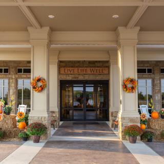 An inviting building entrance decorated with autumn-inspired wreaths, pumpkins, and colorful mums.
