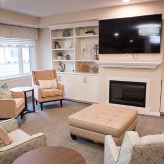 A cozy living room with comfortable seating, a television mounted above a fireplace, and a bookshelf.