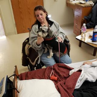 A woman in a wheelchair holding a small dog during a visit in a hospital room.
